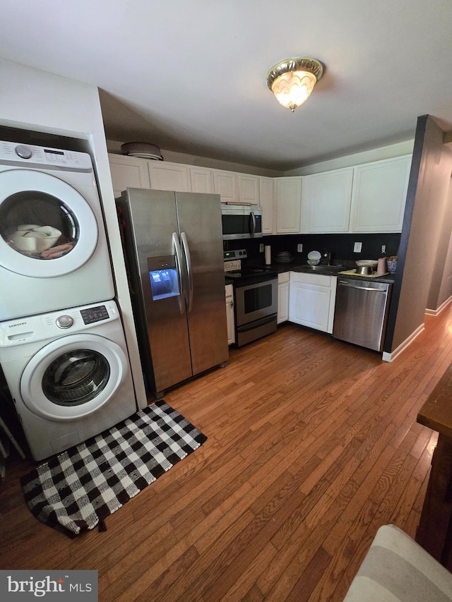 214 Dennison St, Colonial Beach, VA 22443 - kitchen with appliances with stainless steel finishes, stacked washer / dryer, dark countertops, white cabinets, and hardwood / wood-style flooring