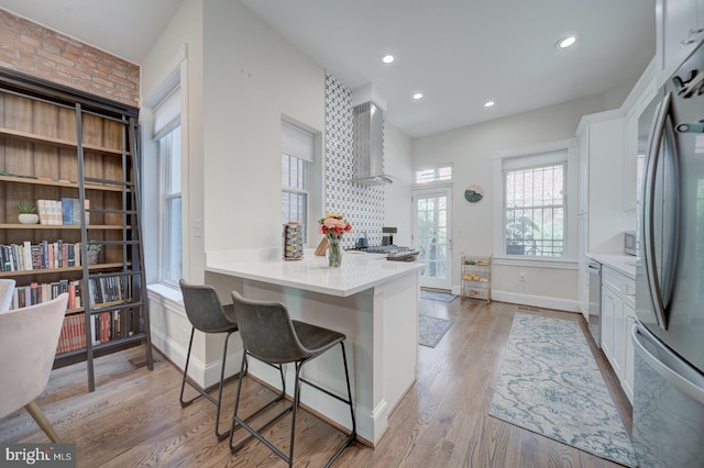 1842 N Capitol St NW, Washington, DC 20002 - kitchen with wall chimney range hood, stainless steel appliances, white cabinetry, a breakfast bar, and recessed lighting
