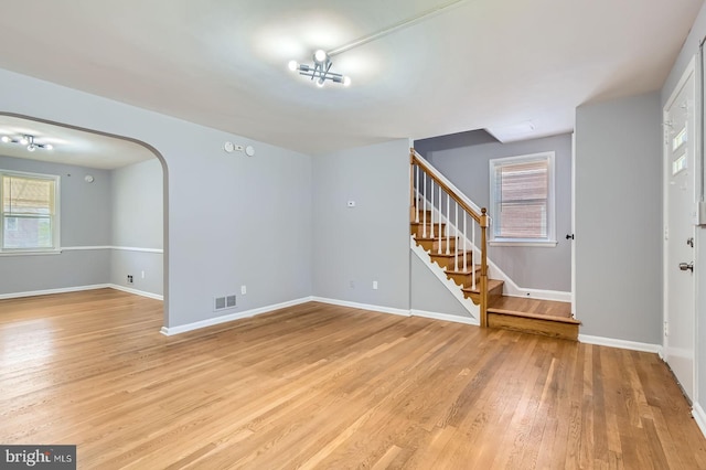 3401 Woodring Ave, Baltimore, MD 21234 - unfurnished living room featuring stairway, light wood-style flooring, plenty of natural light, and arched walkways