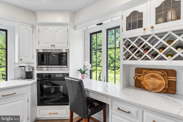 1263 Argyle Rd, Berwyn, PA 19312 - kitchen with black oven, stainless steel microwave, white cabinets, light stone countertops, and crown molding
