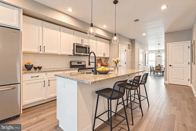 1508 N Eden St, Baltimore, MD 21213 - kitchen featuring stainless steel appliances, light wood-style flooring, white cabinetry, light stone countertops, and a kitchen island with sink