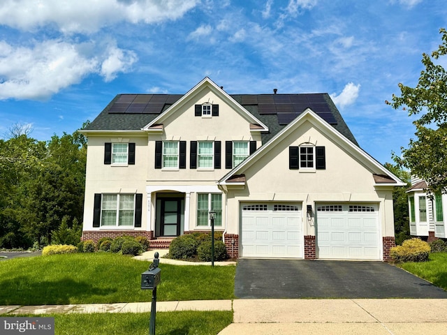 43616 Habitat Cir, Leesburg, VA 20176 - view of front of home with brick siding, asphalt driveway, stucco siding, roof mounted solar panels, and a front yard