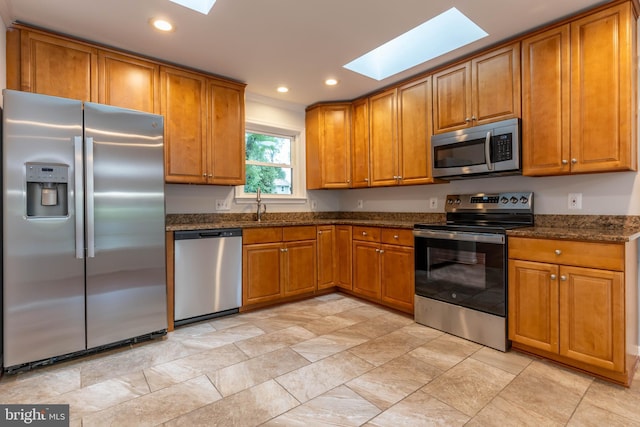 10311 Poe Dr, Manassas, VA 20110 - kitchen featuring appliances with stainless steel finishes, a skylight, brown cabinetry, dark stone counters, and recessed lighting