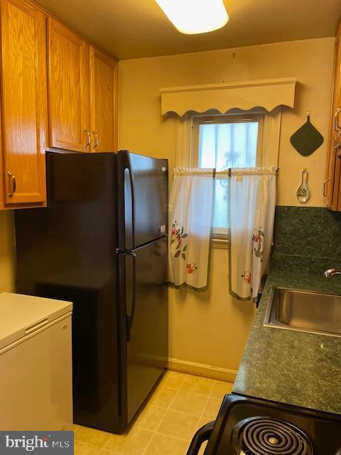 6813 10th Ave, Takoma Park, MD 20912 - kitchen featuring freestanding refrigerator, brown cabinetry, dark countertops, and stove