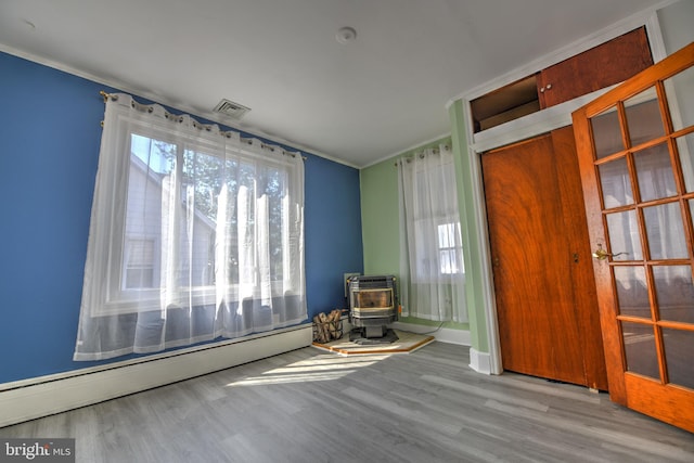 5417 Wasena Ave, Baltimore, MD 21225 - unfurnished room featuring a baseboard radiator, a wood stove, wood finished floors, and crown molding