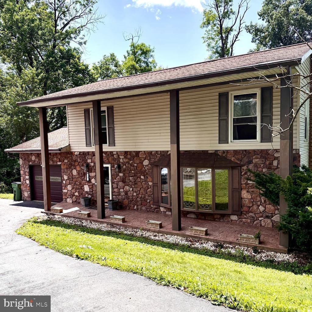 24 Wagner Cir, Hummelstown, PA 17036 - view of front of property featuring stone siding, an attached garage, roof with shingles, asphalt driveway, and a front lawn