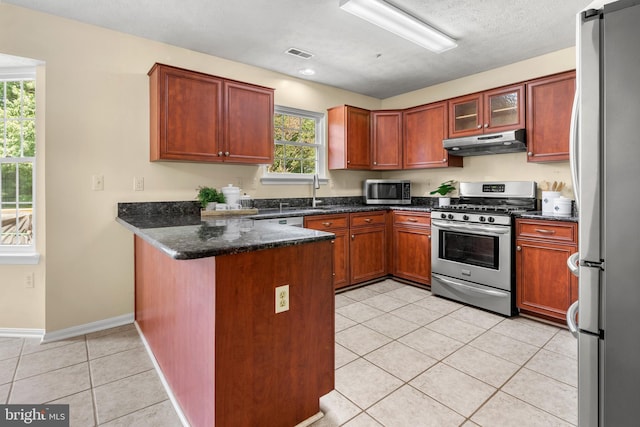 2508 Smoketree Ln, Crofton, MD 21114 - kitchen with appliances with stainless steel finishes, under cabinet range hood, a peninsula, light tile patterned floors, and dark stone countertops