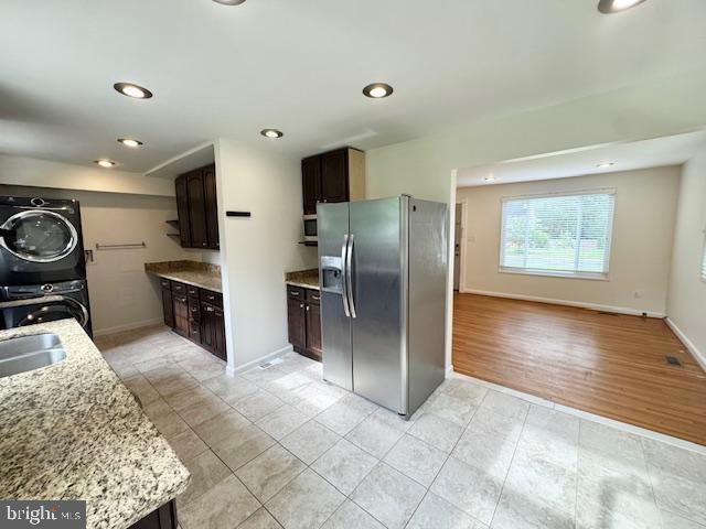 3814 Jancie Rd, Fairfax, VA 22030 - kitchen with stainless steel fridge with ice dispenser, stacked washer and clothes dryer, light tile patterned floors, dark brown cabinets, and light stone counters
