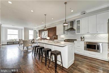 3624 10th St NW Unit 4, Washington, DC 20010 - kitchen featuring wall chimney range hood, stainless steel microwave, crown molding, an island with sink, and white cabinets