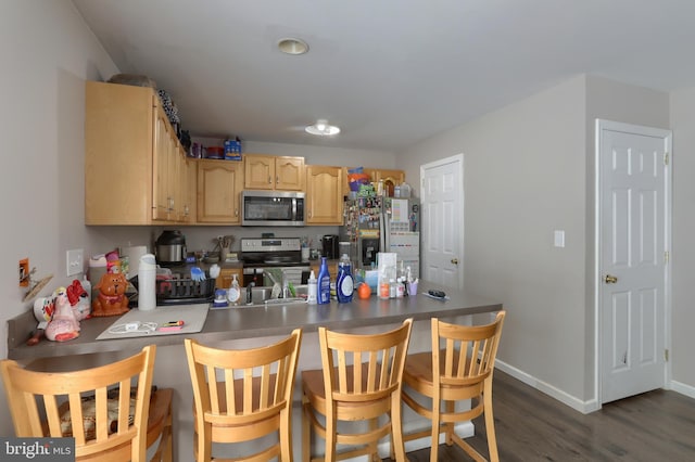 206 Lighthouse Dr, Jonestown, PA 17038 - kitchen with stainless steel appliances, a peninsula, light brown cabinetry, dark wood-style flooring, and a kitchen bar