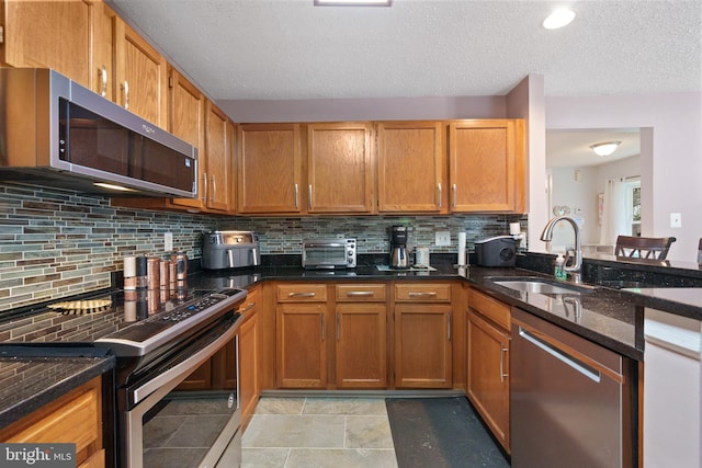 11590 Mohican Rd, Woodbridge, VA 22192 - kitchen with appliances with stainless steel finishes, dark stone counters, backsplash, a textured ceiling, and brown cabinetry