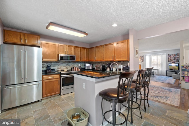 11590 Mohican Rd, Woodbridge, VA 22192 - kitchen featuring appliances with stainless steel finishes, dark countertops, a textured ceiling, a kitchen bar, and tasteful backsplash