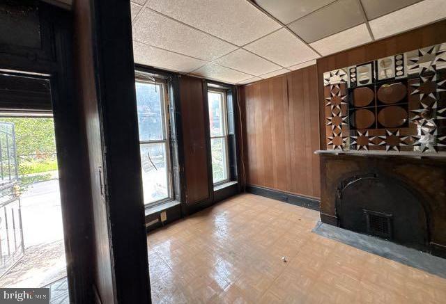 324 Fulton Ave, Baltimore, MD 21223 - unfurnished living room with healthy amount of natural light, wood walls, and a paneled ceiling