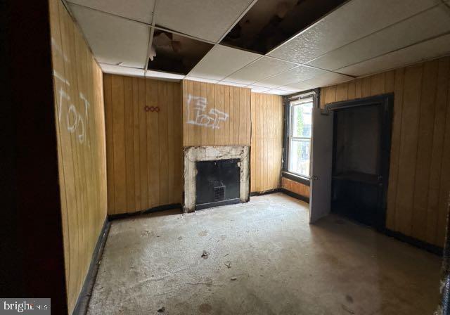 324 Fulton Ave, Baltimore, MD 21223 - unfurnished living room featuring wooden walls, a fireplace, and a drop ceiling