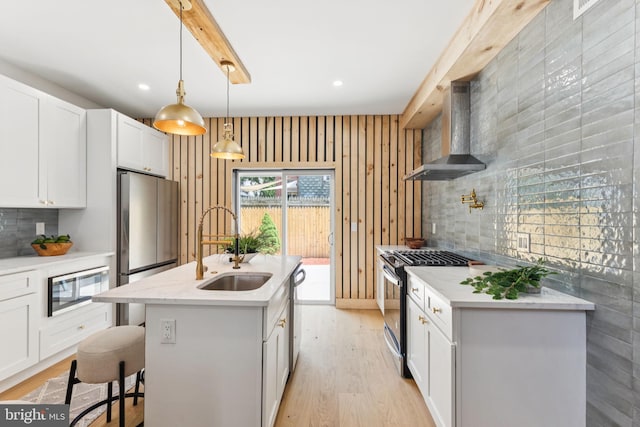 2165 E Gordon St, Philadelphia, PA 19125 - kitchen featuring wall chimney range hood, appliances with stainless steel finishes, tasteful backsplash, an island with sink, and light wood finished floors