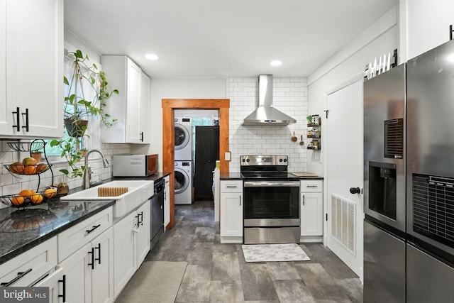 1900 Philadelphia Pike, Claymont, DE 19703 - kitchen with appliances with stainless steel finishes, wall chimney range hood, stacked washer / dryer, backsplash, and white cabinets
