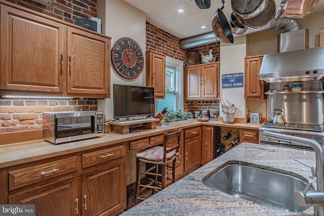 407 N 8th St, Allentown, PA 18102 - kitchen with stainless steel microwave, wall chimney exhaust hood, brown cabinetry, light stone countertops, and brick wall