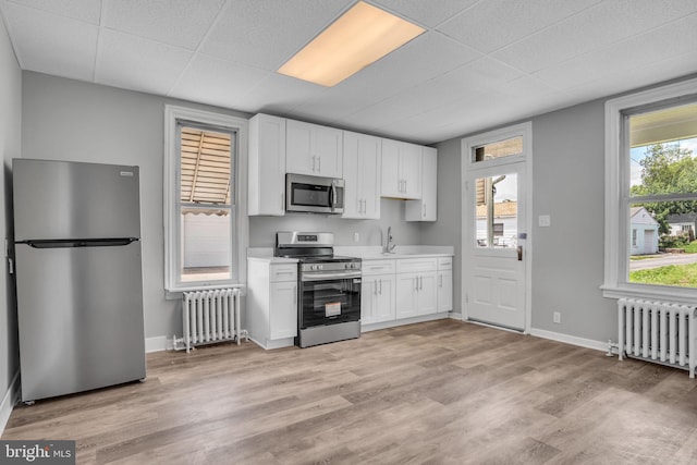345-347 W Penn St, Carlisle, PA 17013 - kitchen featuring stainless steel appliances, radiator, light countertops, white cabinets, and a paneled ceiling