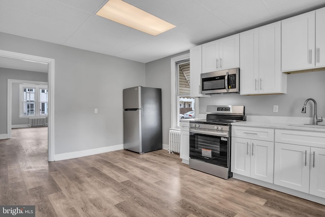 345-347 W Penn St, Carlisle, PA 17013 - kitchen with stainless steel appliances, radiator heating unit, white cabinets, and light wood finished floors