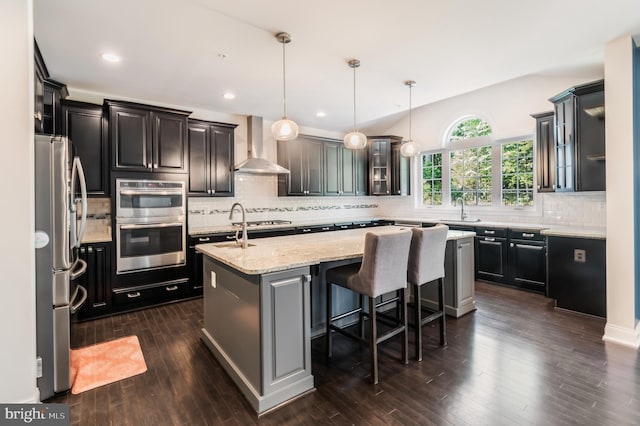 8266 Saint Francis Dr, Severn, MD 21144 - kitchen featuring wall chimney exhaust hood, appliances with stainless steel finishes, an island with sink, backsplash, and glass insert cabinets