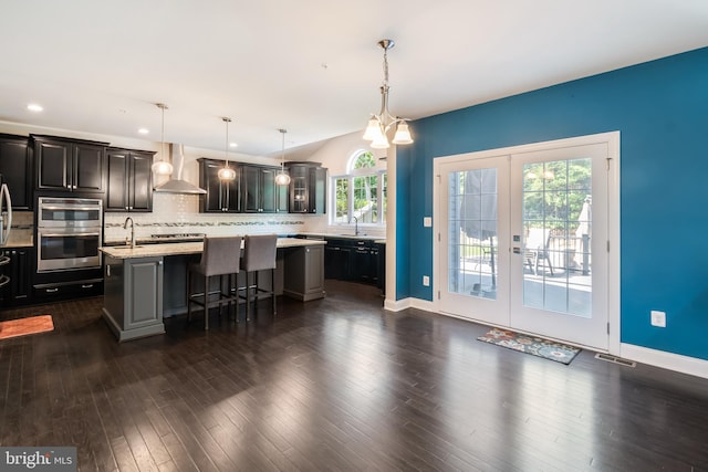 8266 Saint Francis Dr, Severn, MD 21144 - kitchen with wall chimney exhaust hood, stainless steel double oven, a breakfast bar, decorative backsplash, and an island with sink