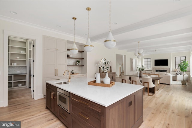 2724 N Dinwiddie St, Arlington, VA 22207 - kitchen with stainless steel microwave, light wood-style floors, open shelves, a center island with sink, and hanging light fixtures