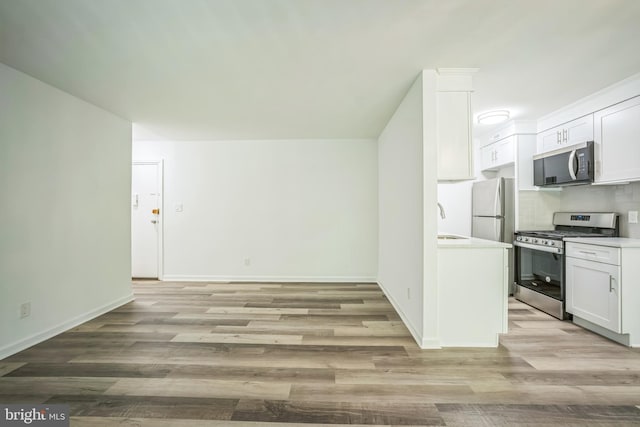 4939 Americana Dr Unit 106, Annandale, VA 22003 - kitchen featuring stainless steel gas stove, freestanding refrigerator, white cabinetry, light wood-type flooring, and light countertops