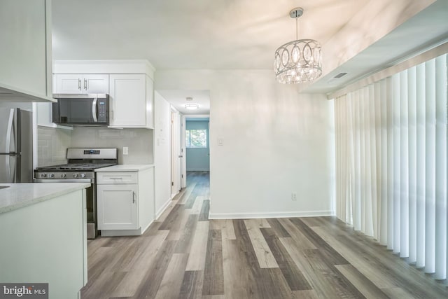 4939 Americana Dr Unit 106, Annandale, VA 22003 - kitchen featuring stainless steel appliances, white cabinetry, light wood finished floors, decorative backsplash, and a chandelier