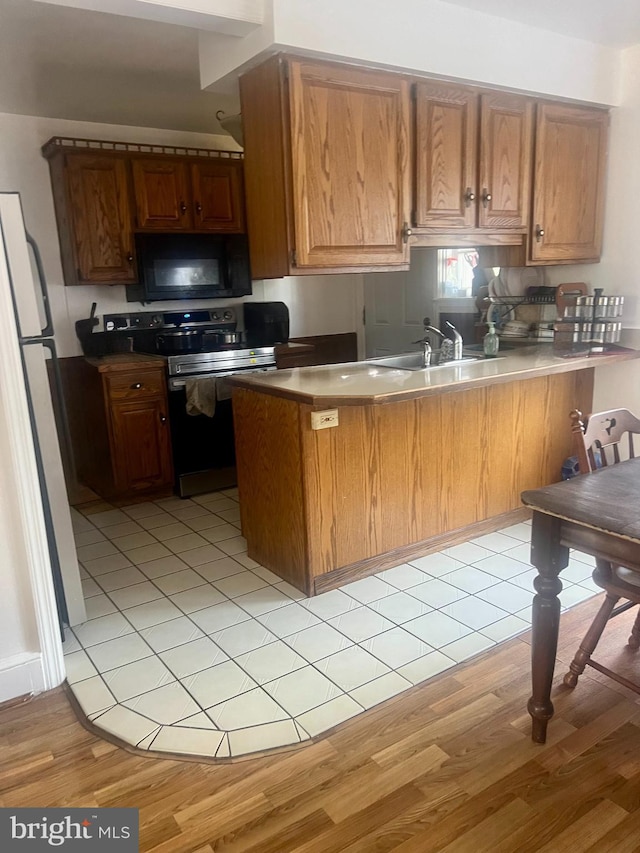 743 E Madison St, Lancaster, PA 17602 - kitchen featuring black microwave, a peninsula, stainless steel range with electric stovetop, freestanding refrigerator, and light wood-type flooring