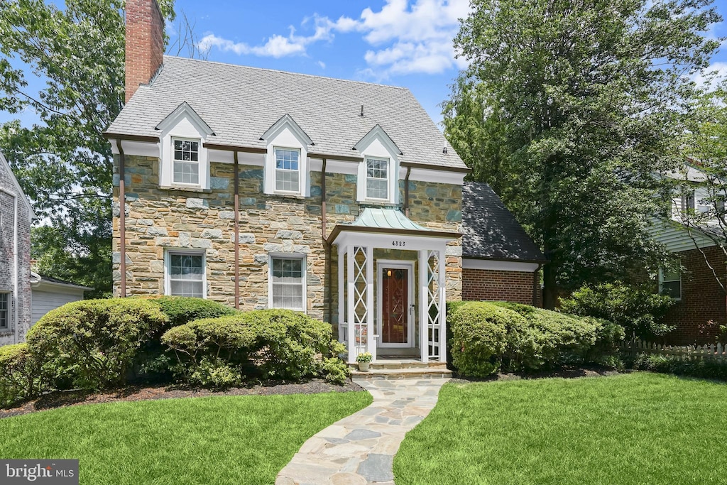 4323 Warren St NW, Washington, DC 20016 - view of front facade featuring stone siding, a chimney, a front yard, and a high end roof