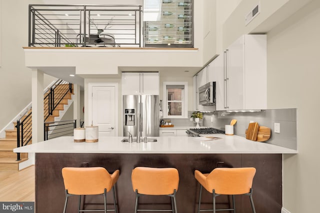 2431 Ontario Rd NW Unit 4, Washington, DC 20009 - kitchen featuring stainless steel appliances, a towering ceiling, white cabinets, a kitchen breakfast bar, and light countertops