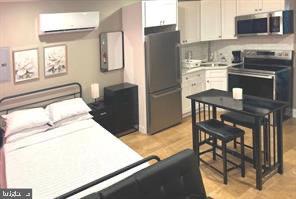2647 N 17th St, Philadelphia, PA 19132 - kitchen with stainless steel appliances, an AC wall unit, light countertops, white cabinets, and light wood-style floors