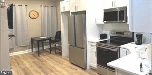 2647 N 17th St, Philadelphia, PA 19132 - kitchen featuring stainless steel appliances, white cabinets, light wood-type flooring, and light countertops