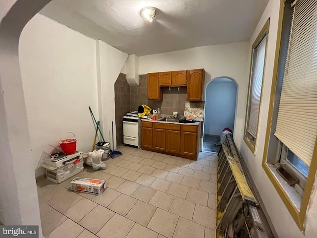706 W Butler St, Philadelphia, PA 19140 - kitchen with arched walkways, tasteful backsplash, brown cabinets, light tile patterned flooring, and light countertops