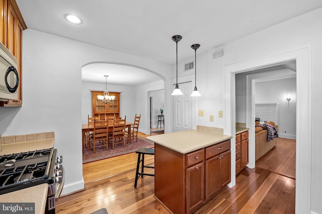 206 E Lake Ave, Baltimore, MD 21212 - kitchen featuring arched walkways, brown cabinetry, wood-type flooring, stainless steel appliances, and decorative light fixtures