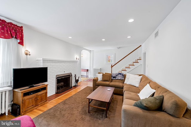 206 E Lake Ave, Baltimore, MD 21212 - living room with radiator heating unit, light wood-type flooring, arched walkways, a brick fireplace, and stairway