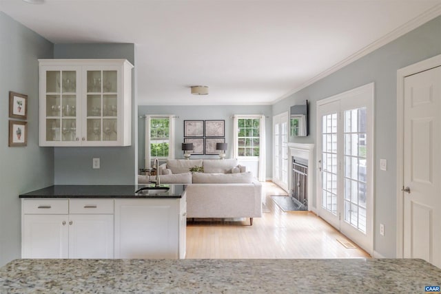 325 Heron Ln, Charlottesville, VA 22903 - kitchen with light wood finished floors, white cabinets, glass insert cabinets, a fireplace with raised hearth, and crown molding