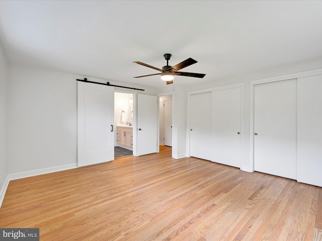 1020 Wyomissing Blvd, Wyomissing, PA 19610 - unfurnished bedroom with two closets, a barn door, light wood-style floors, ceiling fan, and connected bathroom