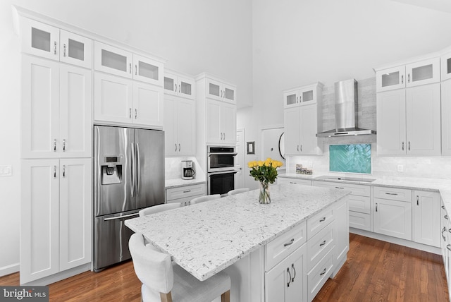 10111 Ballynahown Cir, Fairfax, VA 22030 - kitchen with appliances with stainless steel finishes, wall chimney exhaust hood, a towering ceiling, a kitchen island, and backsplash