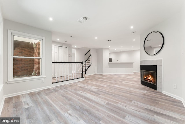 12560 Kempston Ln, Woodbridge, VA 22192 - unfurnished living room featuring a tiled fireplace, light wood-type flooring, stairs, and recessed lighting