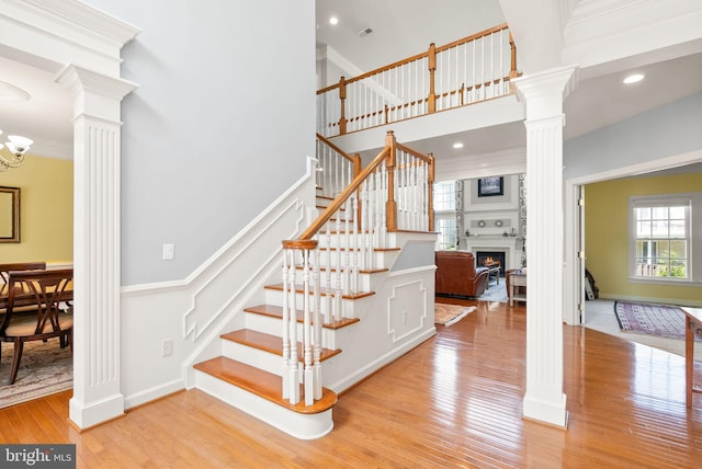 14512 Penderlea Ct, Gainesville, VA 20155 - stairs with decorative columns, a warm lit fireplace, a towering ceiling, wood finished floors, and a chandelier