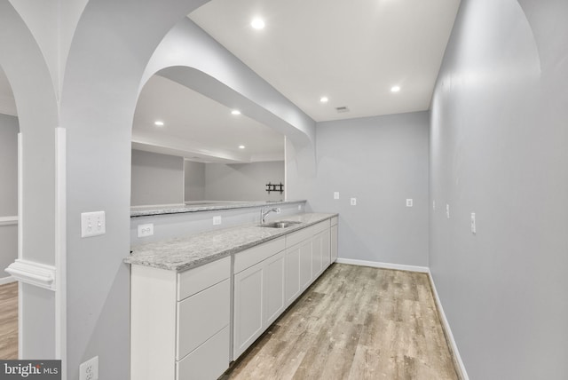 14512 Penderlea Ct, Gainesville, VA 20155 - kitchen with light wood-style floors, white cabinetry, light stone countertops, arched walkways, and recessed lighting