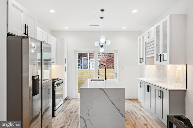 3084 Weikel St, Philadelphia, PA 19134 - kitchen featuring stainless steel appliances, light wood finished floors, a center island with sink, light stone countertops, and white cabinetry