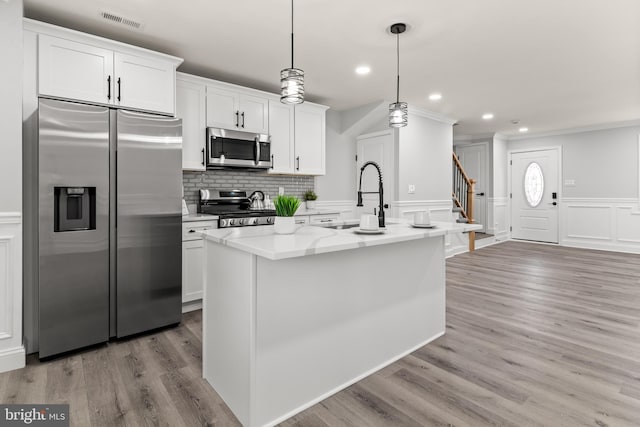 233 S Clinton St, Baltimore, MD 21224 - kitchen featuring stainless steel appliances, an island with sink, white cabinetry, a decorative wall, and crown molding