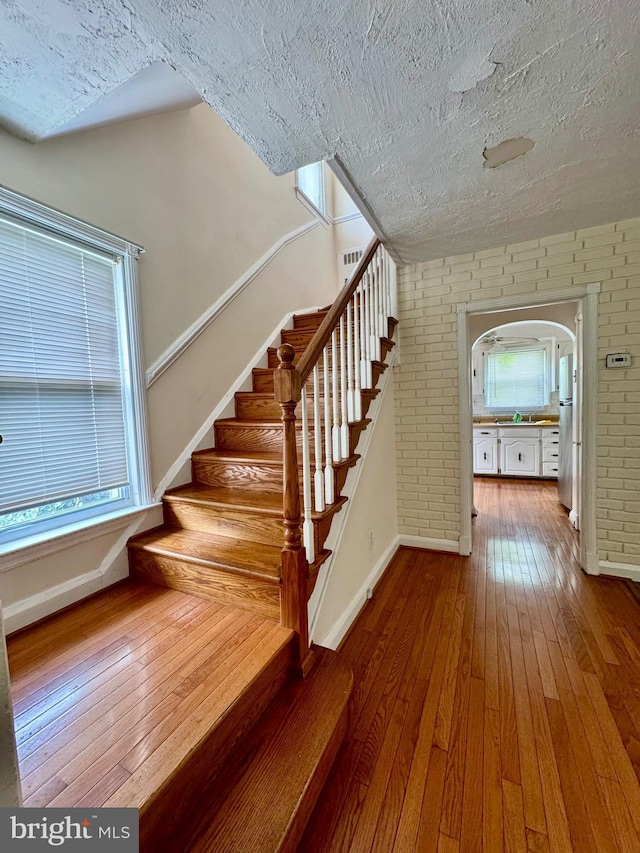 3913 Loch Raven Blvd, Baltimore, MD 21218 - stairs with hardwood / wood-style flooring, a textured ceiling, and brick wall