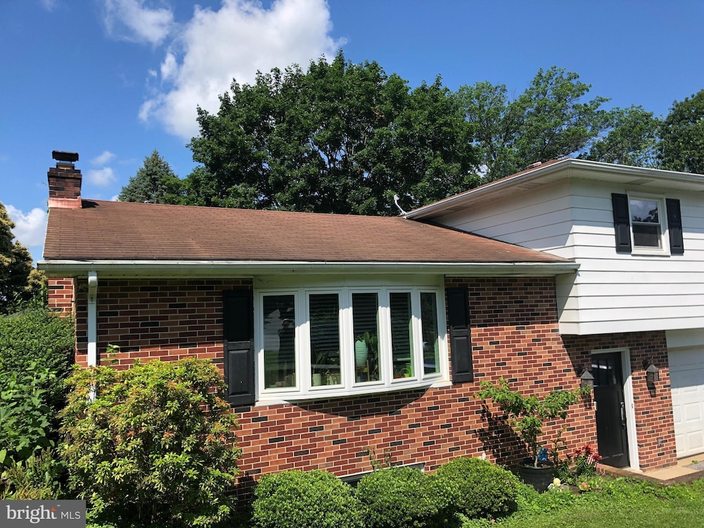 2714 Whitney Dr, York, PA 17402 - view of side of home with brick siding, a chimney, and a garage