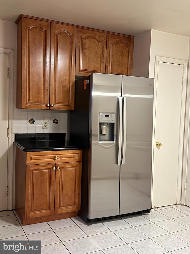 12130 Ambleside Dr, Potomac, MD 20854 - kitchen featuring stainless steel fridge with ice dispenser, dark countertops, brown cabinetry, light tile patterned floors, and tasteful backsplash