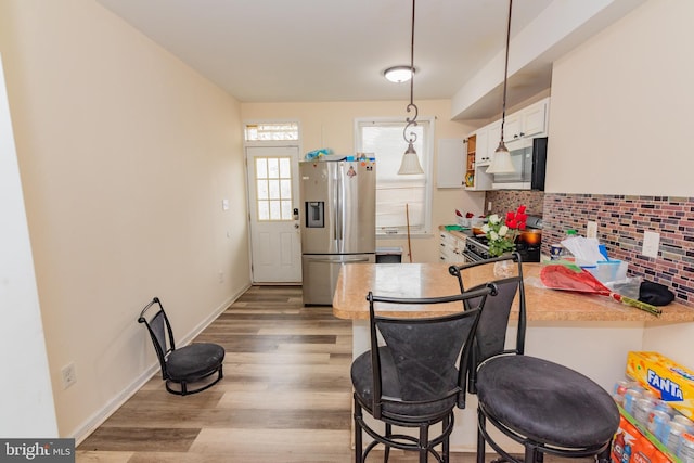 16 S Kresson St, Baltimore, MD 21224 - kitchen with appliances with stainless steel finishes, wood finished floors, tasteful backsplash, decorative light fixtures, and a peninsula