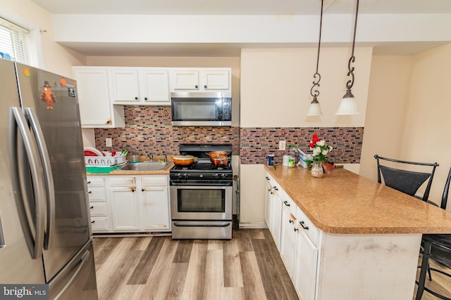 16 S Kresson St, Baltimore, MD 21224 - kitchen featuring stainless steel appliances, a peninsula, white cabinets, and light wood-style flooring