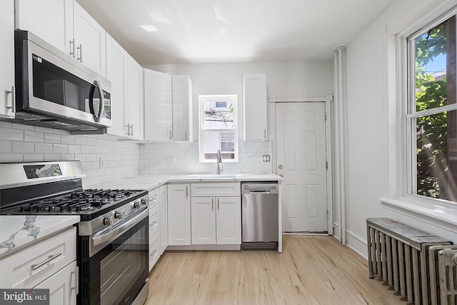 1439 S 28th St, Philadelphia, PA 19146 - kitchen featuring appliances with stainless steel finishes, radiator heating unit, light wood-type flooring, backsplash, and white cabinetry